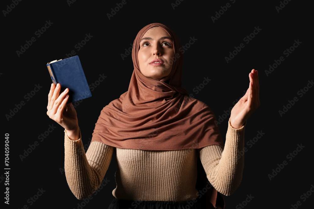 Wall mural Young Muslim woman with Koran praying on black background