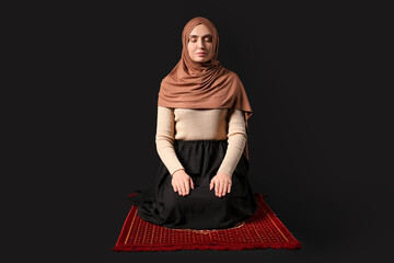 Young Muslim woman praying on black background