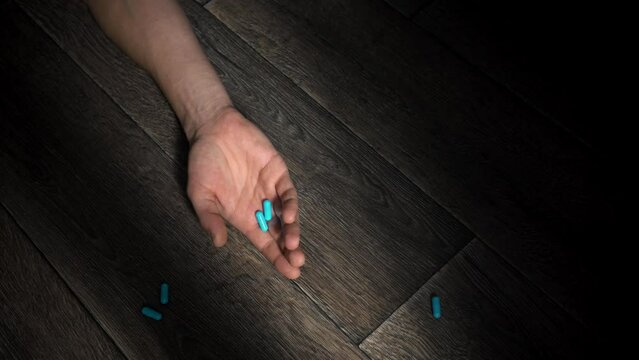 A man's hand falls to the floor, dropping pills. A person loses consciousness after taking medication. Concept of social problems of drug overdose or commit suicide.