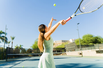 Latin woman seen from behind doing a good tennis serve