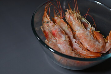 frozen king prawns with head not peeled in shell in transparent plate on gray background 
