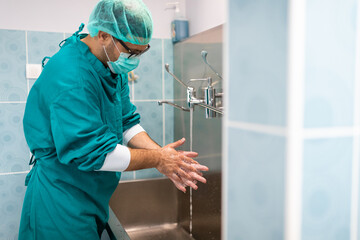Side view photo of male surgeon with eyeglasses professionally dressed in operating gown washing...