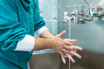 Closeup photo of male hands with soap under running water. Medical professional scrubbing hands...