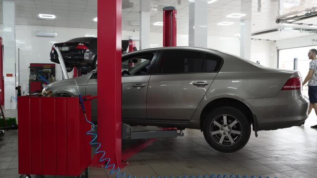 Vehicle suspended on hoist in auto repair shop for maintenance. Mechanic inspects car on lift, fixing undercarriage. Professional garage, tech work, service station with elevated sedan.