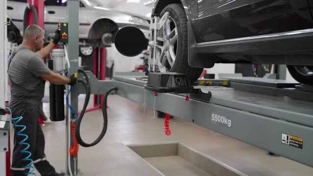 Auto mechanic aligns car wheels with high-precision equipment in garage. Expert conducts vehicle maintenance, ensures proper alignment for safety. Car raised on lift for accurate servicing.