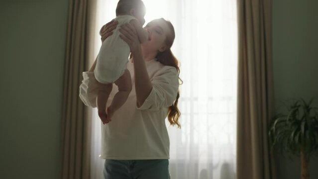 Mother picks up her newborn baby from the bed. Concept of Childhood, new Life, parenthood, maternity, motherhood. Happy mother picks up neonate toddler from bed. Cinematic advertisement for baby care