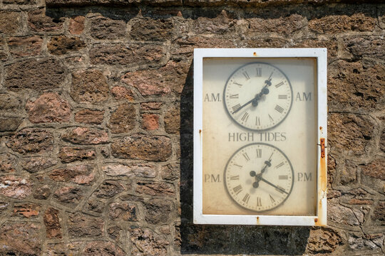 An old, vintage tide clock shows the relevant high and low tide times at Budleigh Salterton beach, Devon, UK
