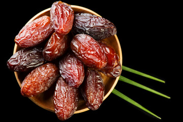 Dates fruit. Date fruits with palm tree leaf, in a wooden bowl, on black background. Medjool dates close up. Top view. 