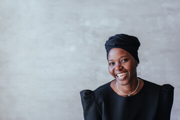 smiling woman in a headscarf posing with a neutral expression against concrete wall with empty...