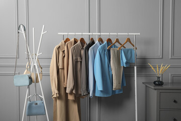 Rack with different stylish women`s clothes and bags near grey wall