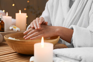 Woman soaking her hands in bowl of water at table, closeup. Spa treatment