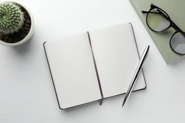 Open notebook, pen, glasses and cactus on white wooden table, flat lay. Space for text