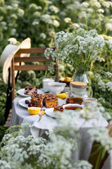 Tea time with sweet homemade cherry cake and herbal beverage in summer garden outdoors. Table covered with linen tablecloth, white porcelain cups. English style