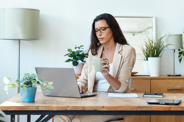 Beautiful business woman working with laptop while drinking coffee in living room at home.