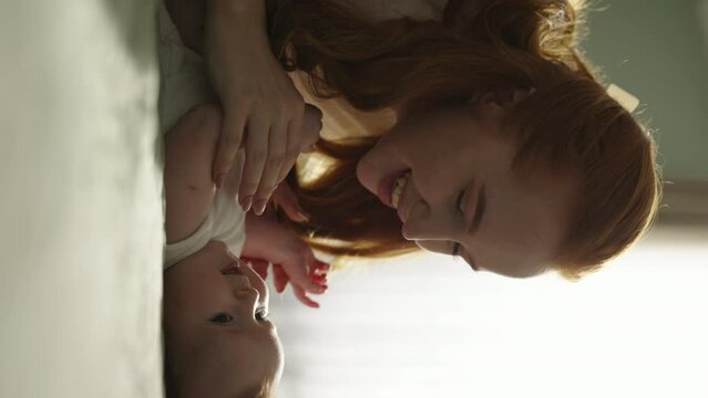 Close up footage of newborn and his mother, lying on back in bed. Caucasian neonate toddler bonding with mom. Mom kisses baby. Concept of childhood parenthood. Cinematic AD, vertical video