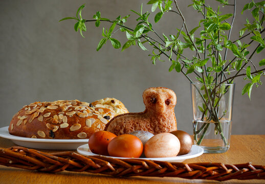 Easter still life containing a small lamb cake, painted eggs, traditional Czech Easter sweet cake called "mazanec", an Easter whip and green twigs in a vase