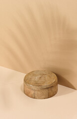 Round wooden platform, shadow from a palm leaf on a brown background.