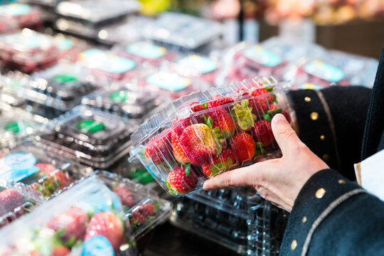 Person buying fresh strawberries at the farmer's market. Hand holding a container of fresh red strawberries.