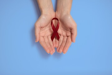Woman holding red ribbon as symbol of World Cancer Day, on blue background, cancer awareness sign