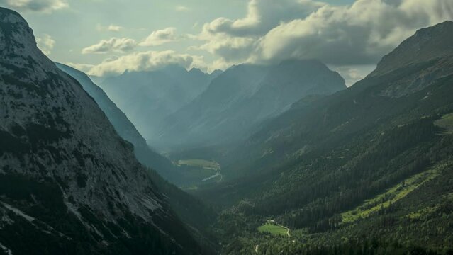 Timelapse of moving clouds and sunbeams over valley in Karwendel mountains during sunny blue sky day in summer from above, sunbeams breaking through white clouds in the sky, Tyrol Austria.