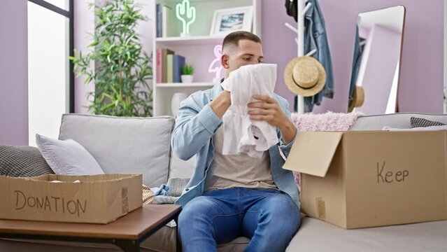 A young man sorts clothing into 'donation' and 'keep' boxes in a cozy, modern living room.