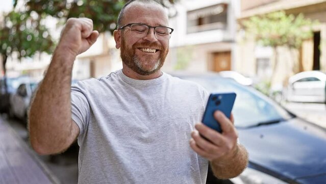 Eureka! cheerful middle-aged caucasian man with beard, firstly celebrating using smartphone on outdoor city street, texting a winning message!