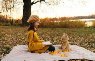 Little girl reading a book to her friend Winnie the Pooh. Autumn vibe. 