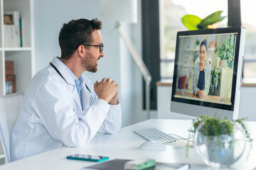 Mature male doctor talking in a video call with computer in the consultation.