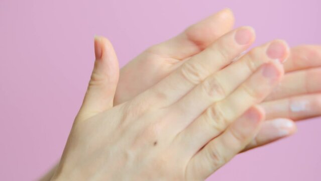 Woman applying nourishing cream on hand skin. Female hands care. Hands close up on pink background. Hand protection from frostbite
