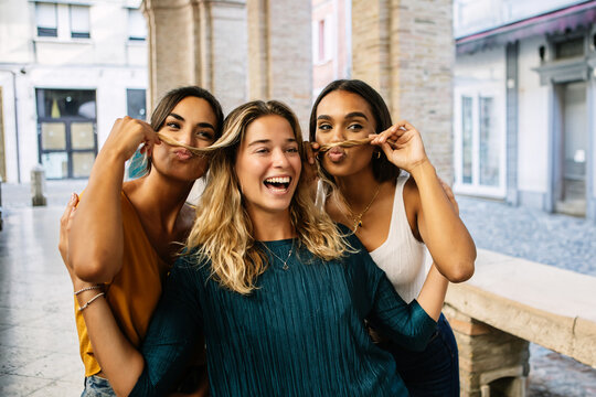 Three happy diverse women enjoying summer vacation taking photo at city street. Funny female friends posing for a photograph standing together. Friendship, unity and holidays concept.
