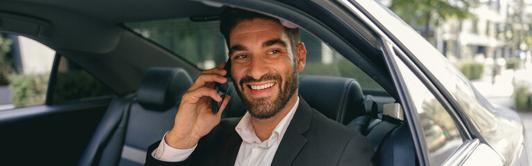 Smiling businessman talking phone with client while sitting on car backseats. High quality photo