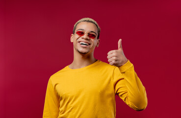 Positive man makes hand sign like, thumbs up gesture. Happy student guy on red