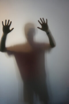Man with raised hands silhouette behind frosted glass