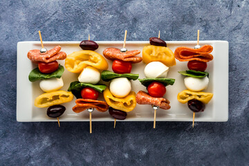 A platter of colourful antipasto skewers against a blue background.