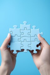 Light blue puzzle pieces being held together by a person's hands against a light blue background,