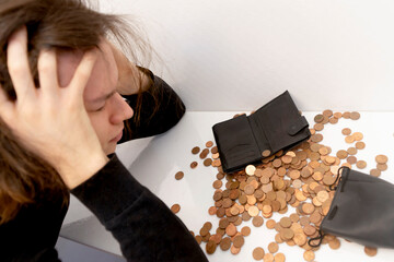 a young man with stressful emotions holds his head with his hands over a mountain of small coins...