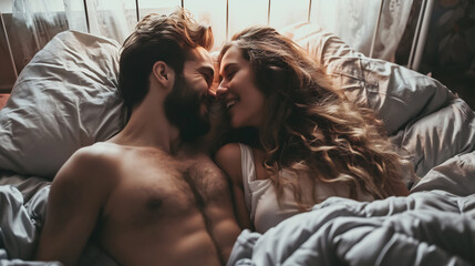 Young beautiful and loving couple wake up while lying on white pillows under the covers on soft white bed at the morning - obrazy, fototapety, plakaty