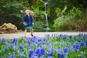 Adorable preschooler girl enjoying nice spring day in park during hyacinth blooming season