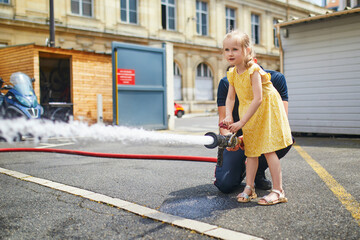 preschooler girl acting like a fireman holding firehose nozzle and splashing water