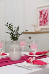 Table setting. Glasses of tasty beverage, plates, pink napkins and vase with green branches in dining room