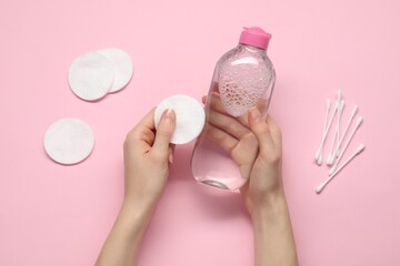 Woman holding makeup remover and cotton pad on pink background, top view