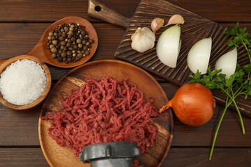 Meat grinder with beef mince, onion, parsley, garlic and spices on wooden table, flat lay