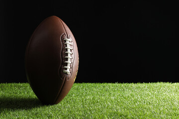 Leather American football ball on green grass against black background. Space for text