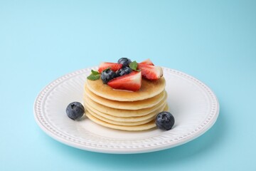 Delicious pancakes with strawberries, blueberries and mint on light blue background
