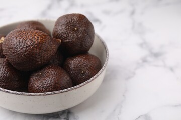 Fresh salak fruits in bowl on white marble table, closeup. Space for text