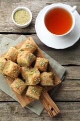 Delicious fresh baklava with chopped nuts and tea on wooden table, flat lay. Eastern sweets