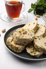 Tasty halva with pistachios served on white tiled table, closeup