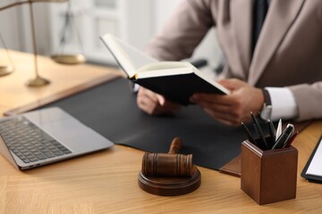 Lawyer reading book at table in office, focus on gavel and pens holder