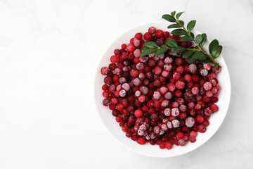 Frozen red cranberries and green leaves on white marble table, top view. Space for text