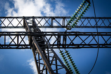 Metal support of a high-voltage power line with insulators on a sunny summer day against a blue sky